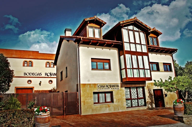 Fachada de Casa Rojanda junto al edificio de Bodegas Rojanda, con galerías de madera y flores en los balcones