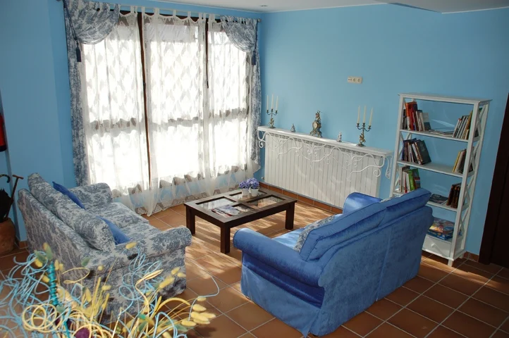 Salón común con sofás azules, estantería y ventanal